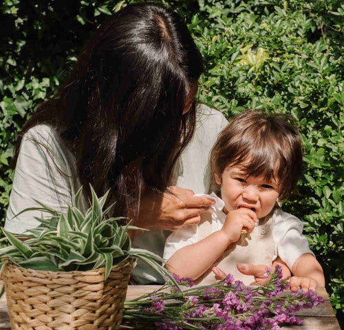 L'image capture un enfant et une mère à une table extérieure, entourés de verdure. L'enfant goûte un aliment et semble ne pas l'apprécier à en juger l'expression de son visage. - Mustela France - 1
